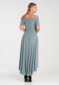 Sukienka bez ramiączek do ziemi w miękkim, jasnoniebieskim materiale. Ma krótkie rękawy, dopasowaną górę i rozkloszowany dół. Widać czarne obcasy.