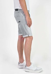 Grijze denim shorts met opgerolde zomen, zijzakken en een zwart label op de tailleband, gecombineerd met witte sneakers met grijze accenten.