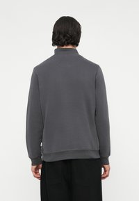 Grauer Pullover mit hohem Kragen, langen Ärmeln und gerippten Bündchen. Glatte Textur mit minimalen Details und einem lockeren Sitz.