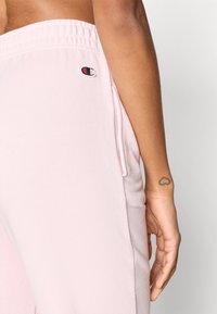 Ανοιχτό ροζ φόρμα από απαλό ύφασμα, με ελαστική μέση και μικρό κεντημένο λογότυπο στην πίσω τσέπη.