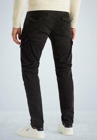 Schwarze Cargo-Hose aus Baumwolle mit seitlichen Taschen und schmaler Passform. Verfügt über Gesäßtaschen und einen sauberen Abschluss an den Säumen. Getragen mit weißen Sneakers.