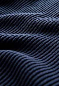 Primer plano de tela de pana azul oscura que muestra costillas elevadas y paralelas, así como suaves ondas texturizadas en el material.