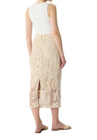 Beige Spitzenrock mit floralen Mustern, knielang, verfügt über einen seitlichen Schlitz für Bewegungsfreiheit. Kombiniert mit einem weißen Tanktop und flachen Sandalen.