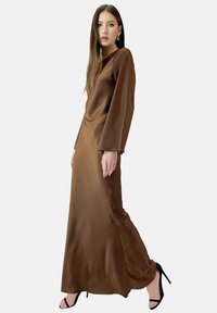 Robe maxi en satin marron avec des manches longues, un col rond et une fente sur le côté. Assortie à des chaussures à talons hauts noires. Texture lisse.