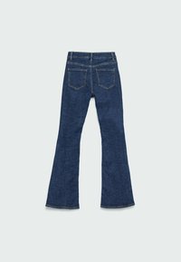 Dzwony z niebieskiego denimu o średnim stanie, z dwoma tylnymi kieszeniami i kontrastowym przeszyciem. Materiał ma gładkie, teksturowane wykończenie.