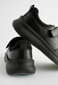 Baskets de sport noires en matériaux cuir et textile, dotées d'un col rembourré, d'une sangle Velcro et d'une semelle en caoutchouc texturé.
