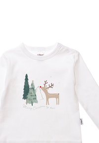 White long-sleeve shirt featuring a reindeer with a red nose, two green trees, and “Merry Christmas my deer” in a delicate font.