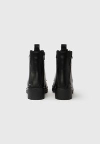 Schwarze Stiefeletten aus Leder mit glatter Textur, ausgestattet mit einem seitlichen Reißverschluss und einem Blockabsatz. Die Rückansicht zeigt den Absatz und die Reißverschlussdetails.