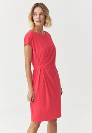 Robe mi-longue de couleur corail vif, confectionnée dans un tissu lisse, avec un col rond et de légères plis à la taille pour ajouter de la texture.