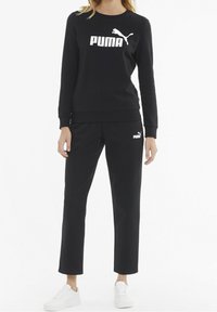 Black sweatshirt and pants made of cotton blend, featuring a large white PUMA logo on the front. Paired with white sneakers.