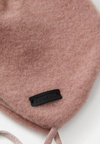 Weicher, strukturierter Staubrosa-Fleece-Stoff mit einem kleinen schwarzen rechteckigen Etikett, auf dem "PURE PURE" steht, in der Nähe der unteren Kante aufgenäht.