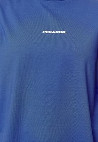 Blaues Baumwoll-T-Shirt mit weichem Material und einem weißen "PEGADOR"-Logo, das mittig auf der Brust platziert ist. Einfaches Design mit kurzen Ärmeln.