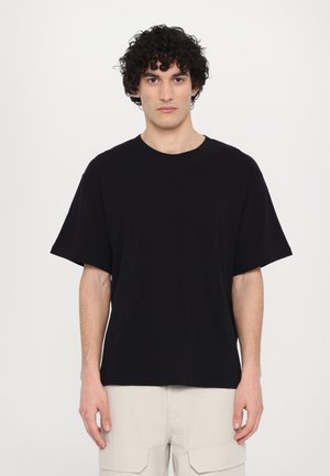 T-shirt noir en coton avec un col rond et des manches courtes, présentant une coupe décontractée et une texture lisse. Design simple sans motifs visibles.