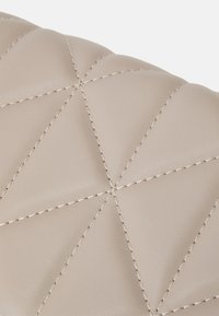 Beige nahka pinta, jossa on vinon saumakuviot, ja joka tarjoaa sileän tekstuurin ja hienovaraisen kiillon.