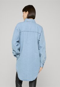 Camicia in denim azzurro chiaro con vestibilità morbida, polsini con bottoni e orlo arrotondato. Presenta un collo a punta e una trama liscia.