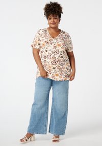 Beige top met bloemenpatroon en korte mouwen in V-hals, gecombineerd met lichtblauwe wijde jeans. Sandalen met blokhakken maken de outfit compleet.