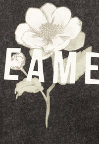 Άσπρο περίγραμμα λουλουδιού με φύλλα και μίσχο που επικαλύπτει έντονα λευκά γράμματα "E A M E" σε σκούρο υφασμάτινο φόντο.