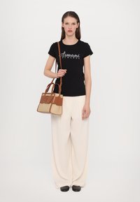 Schwarzes T-Shirt mit "Armani Exchange"-Logo, beige-braune Tasche mit strukturiertem Design, cremefarbene, weit geschnittene Hose, schwarze Schuhe.