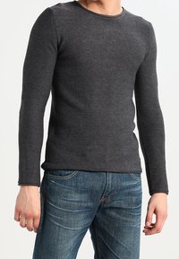 Dunkelgrauer Langarmpullover mit strukturiertem Strickmuster, rundem Ausschnitt und figurbetonter Silhouette, kombiniert mit blauen Jeans.