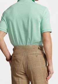 Mint green polo shirt paired with beige checkered trousers, featuring a textured fabric and back pockets with button closures.