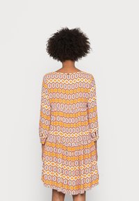 Kleurrijke jurk met een ronde halslijn, lange mouwen en een gelaagde rok. Het ontwerp bevat oranje, roze en zwarte motieven.