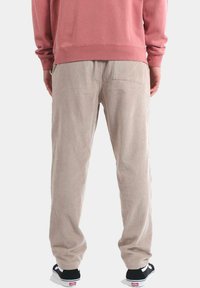 Los pantalones de pana beige presentan un corte relajado con costuras verticales visibles. Combinados con zapatillas negras, el conjunto tiene una apariencia casual.