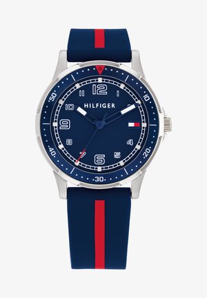 Tommy Hilfiger sat sa s remenom od tamnoplavog silikona, okruglom kućištu od nehrđajućeg čelika, plavom brojčaniku, bijelim oznakama sati, crvenim i bijelim naglascima te funkcijama kronografa.