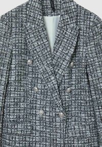 Blazer doppiopetto grigio e bianco con bottoni metallici e colletto a scaldacuore, realizzato in un tessuto tessuto testurizzato.