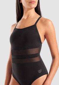 Μαύρο μαγιό με διαφανή οριζόντια πλέγματα. Διαθέτει ρυθμιζόμενους ιμάντες και εφαρμοστή γραμμή. Λογότυπο στη δεξιά κάτω γωνία.