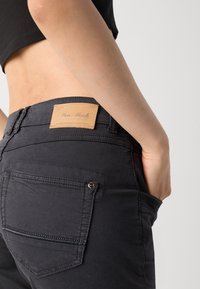 Jean noir avec un patch en cuir embossé du logo à l'arrière, design à cinq poches et détails de couture subtils.