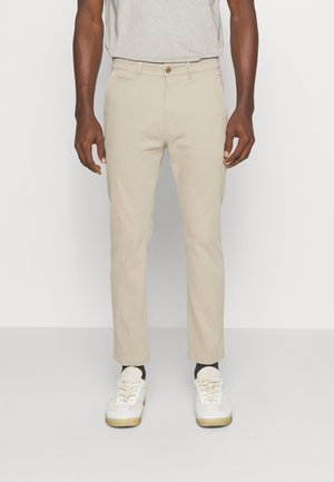 Beige katoenen chinos met een slim fit, rits en knoopsluiting. De stof heeft een zachte textuur en beschikt over zijzakken en een subtiel ontwerp.