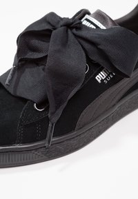 Baskets Puma en daim noir avec un grand nœud en tissu texturé sur fond blanc.