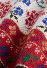 Gros plan sur un tissu en laine texturé avec des motifs traditionnels nordiques tricotés en rouge, blanc, bleu, vert et noir.
