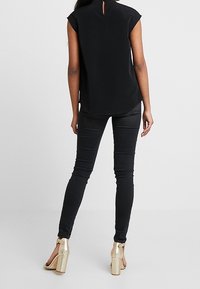 Sort kortærmet bluse med nøglehul bagpå, stylet med slanke sorte jeans og metallisk guld-højhælede sko.