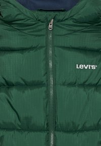 Grüne Pufferjacke mit horizontalem Steppmuster, Reißverschluss und weißem Levi's-Logo. Das Innenfutter besteht aus marineblauem Fleece.