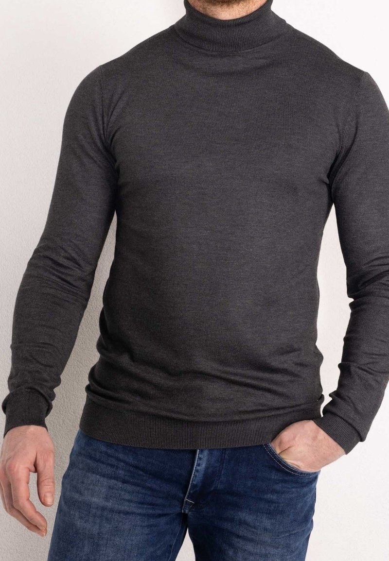 Pull à col roulé gris foncé, col côtelé, manches longues, coupe ajustée, fabriqué dans un matériau doux et extensible, porté avec un jean bleu.