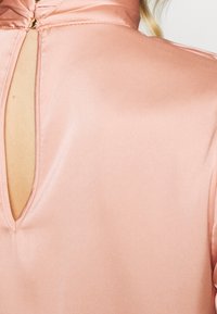Blusa in satin di un rosa chiaro, con piccola apertura a chiave sul retro e colletto alto, dalla texture liscia e dettagli di cucitura pulita.