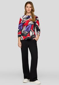 Multicolored top featuring bold floral and abstract patterns in red, purple, and black; paired with black wide-leg pants and white sneakers.