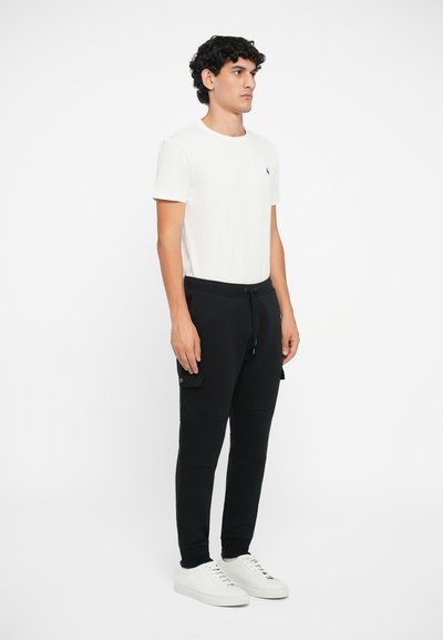 Îmbrăcăminte masculină care include un tricou alb din bumbac și pantaloni jogger negri cu buzunare cargo. Completată cu adidași albi, cu o textură netedă.
