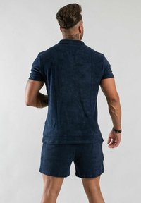 Mörkblå polo skjorta och matchande shorts tillverkade av mjukt, texturerat material. Har en klassisk krage och korta ärmar.