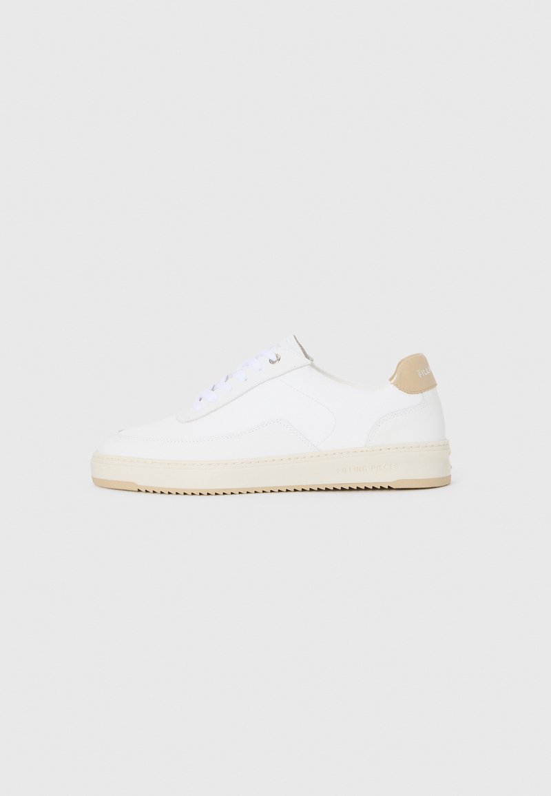 Hvite lave sneakers med overdel i teksturert skinn, kremfarget såle med ribber og en brunt fargeklatt på hælen. Har hvite lisser og logodetalj på hælen.