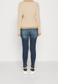 Suéter de punto a rayas beige y blanco con dobladillo acanalado, combinado con jeans ajustados azul oscuro y zapatillas blancas con detalles en negro.