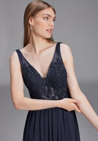 Robe de soirée marine avec un corsage transparent, orné de dentelle florale et de sequins. Présente un décolleté en V profond et une jupe fluide.