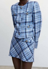 Costume en tweed à carreaux bleu clair et marine, comprenant une veste ajustée avec des boutons argentés et une mini-jupe assortie avec une patte décorative et un bouton.
