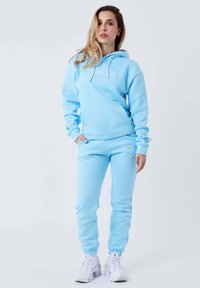 Lyseblå hoodie og matchende sweatpants i blødt stof, med en frontlomme og elastiske manchetter. Pyntet med hvidt logo broderi.