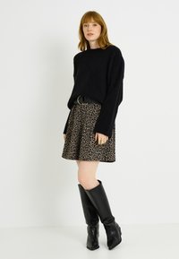 Pull en maille noire oversized, associé à une mini-jupe imprimé léopard, cintré avec une ceinture noire, et des bottes en cuir noir montant aux genoux.