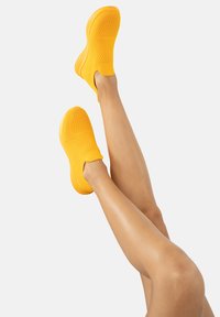 Helle gelbe Slipper mit strukturiertem Obermaterial, ausgestattet mit einer flexiblen Sohle und einem schlanken Design.