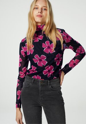 Langmouwige, doorzichtige top met een col, marineblauwe basis en een groot roze bloemenpatroon. Gepaard met donkergrijze jeans met een knoopsluiting.