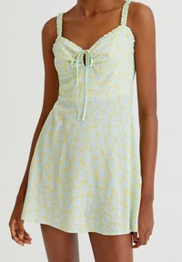 Robe d'été à motifs légers présentant des couleurs jaune pastel et vert menthe, avec un col froncé, des bretelles ajustables et un imprimé floral.