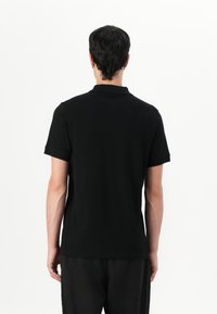 Μαύρο πόλο μπλουζάκι με κοντά μανίκια, κλασικό γιακά, απαλό ύφασμα και εφαρμοστή γραμμή, θέα από το πίσω μέρος σε λευκό φόντο.